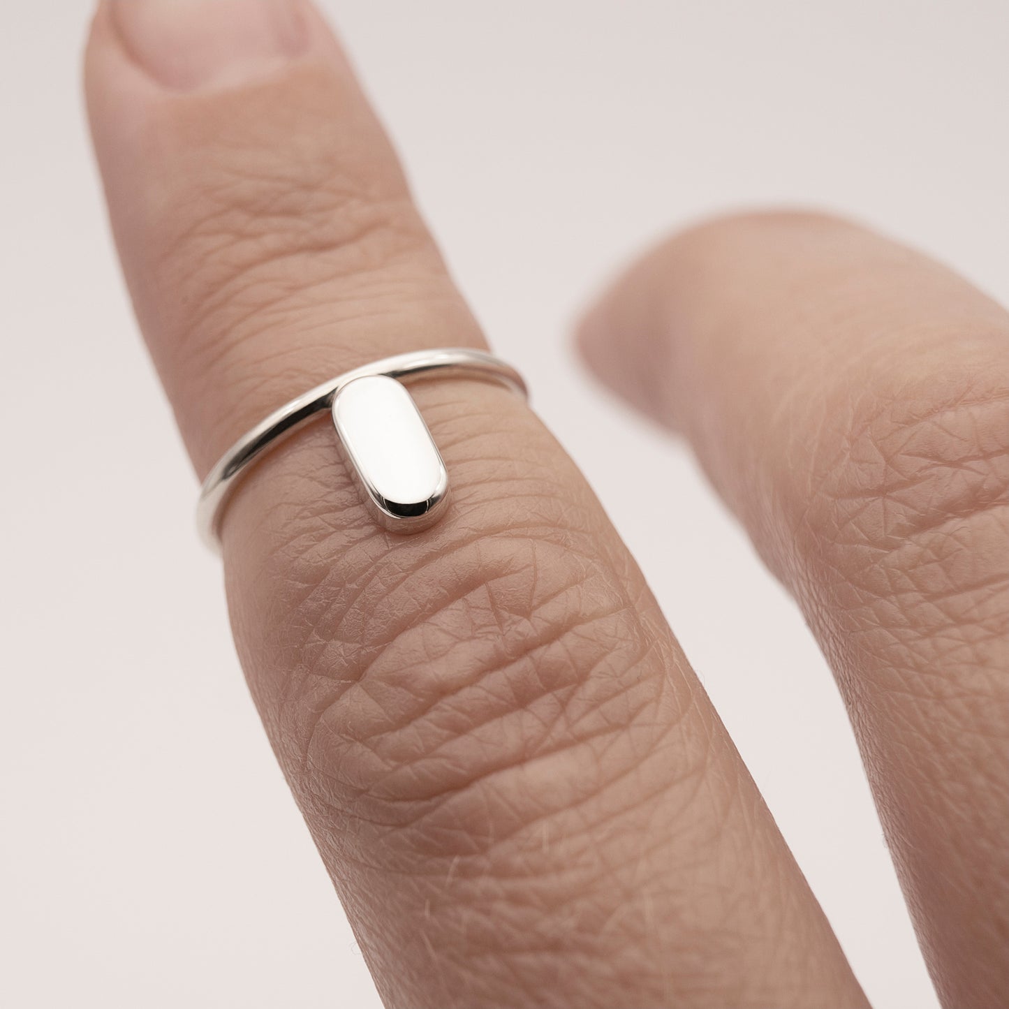 A close-up of a silver ring with a minimalist design and a flat capsule element on a woman's index finger above the knuckle.