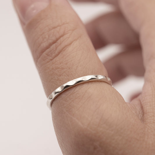 A close-up of a minimalist design thin silver ring with a wavy texture.