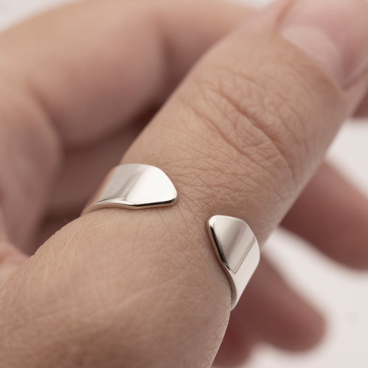A close-up of a minimalist design wide band ring in silver on a woman's thumb.