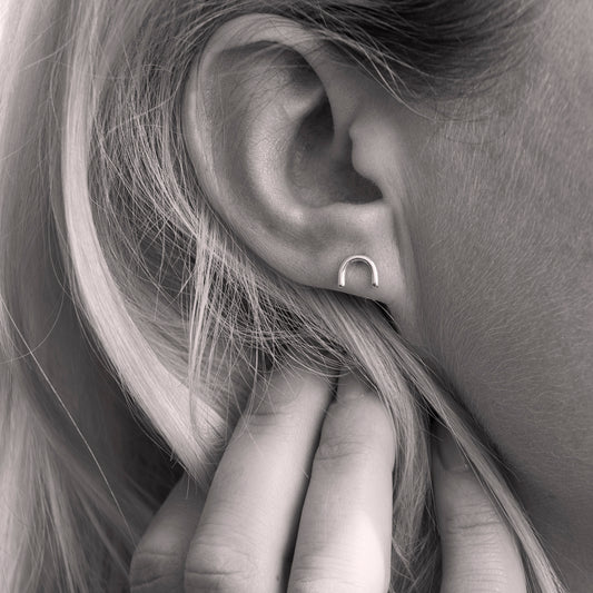 A close-up of a minimalistic silver horseshoe-shaped earring in woman's ear. Black and white.