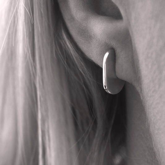 A close up of a minimalist design silver earring in a woman's ear. Black and white.