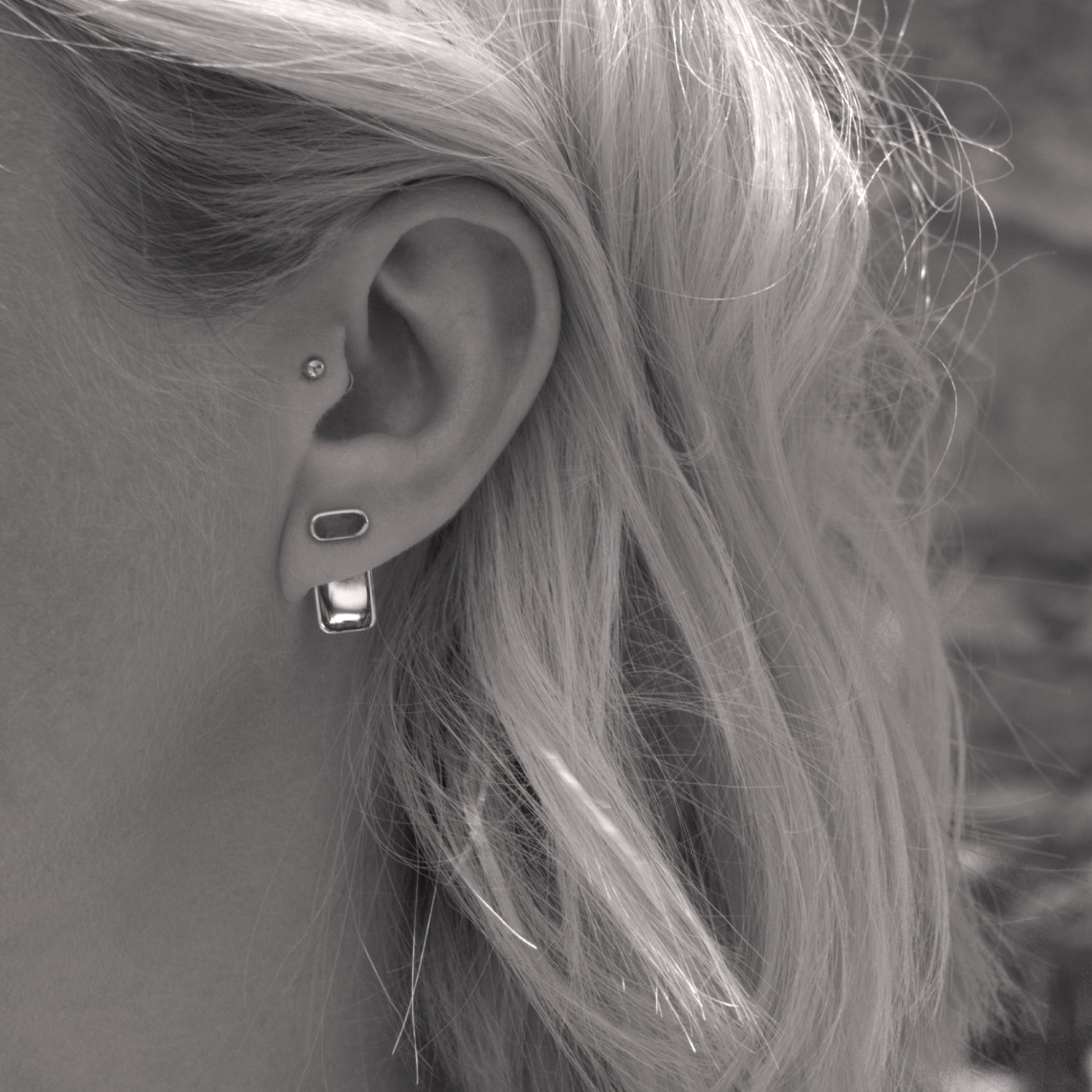 A close-up of a minimalist silver earring in a woman's ear. Black and white.