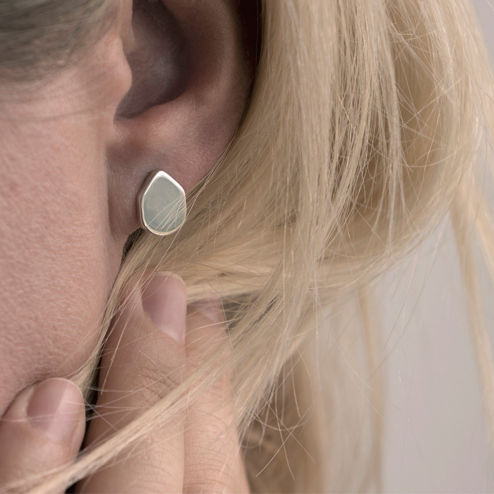 A close-up of a minimalist earring with an organic shape in a woman's ear.