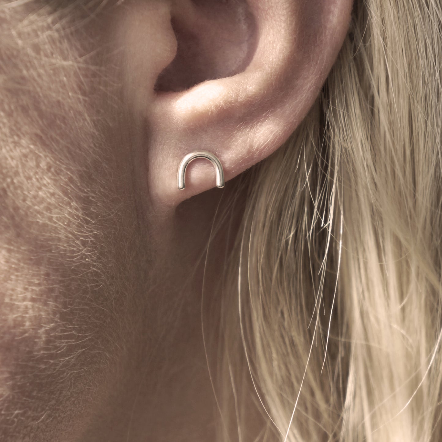 A close-up of a minimalistic silver horseshoe-shaped earring in woman's ear.