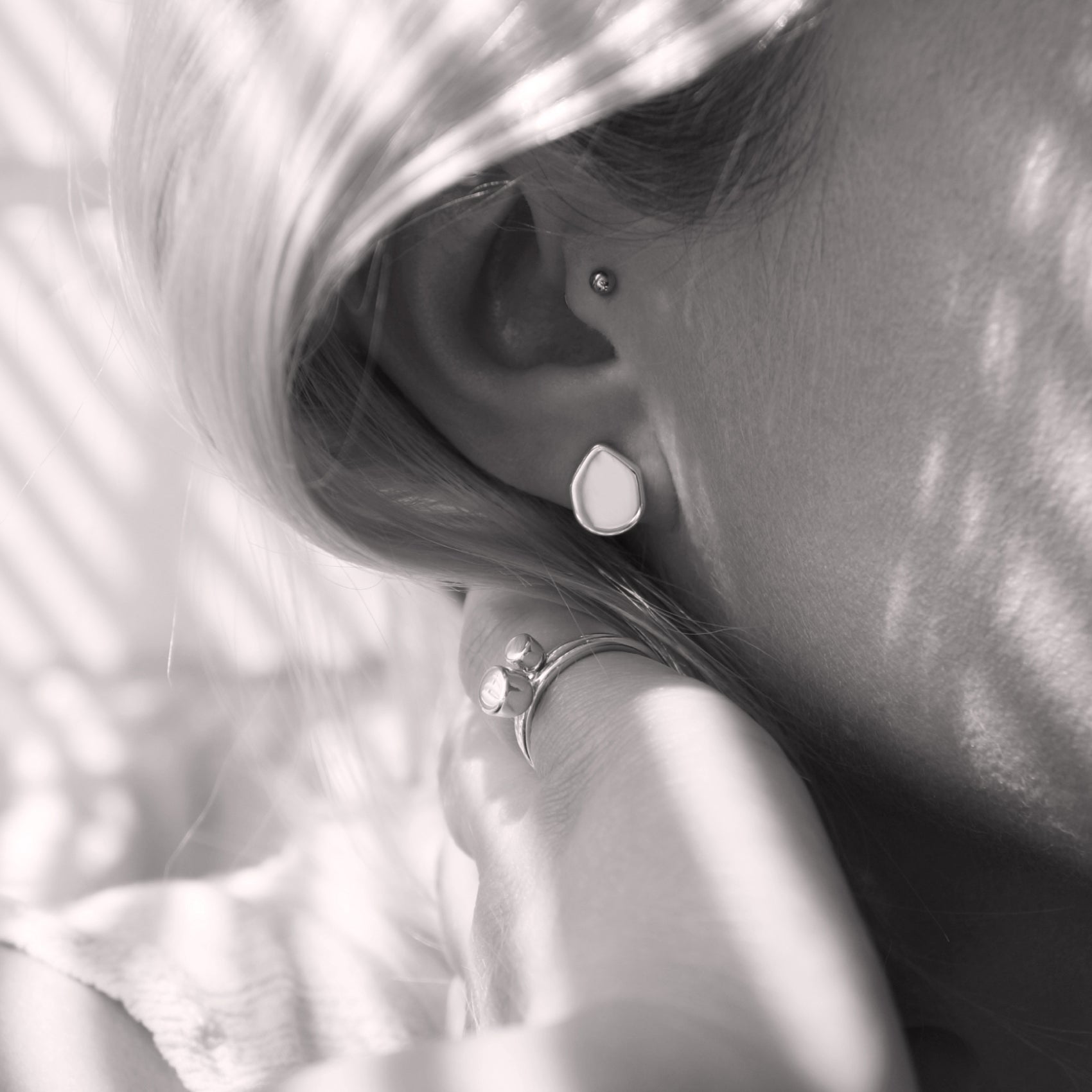 A close-up of a minimalist earring with an organic shape in a woman's ear. Black and white.