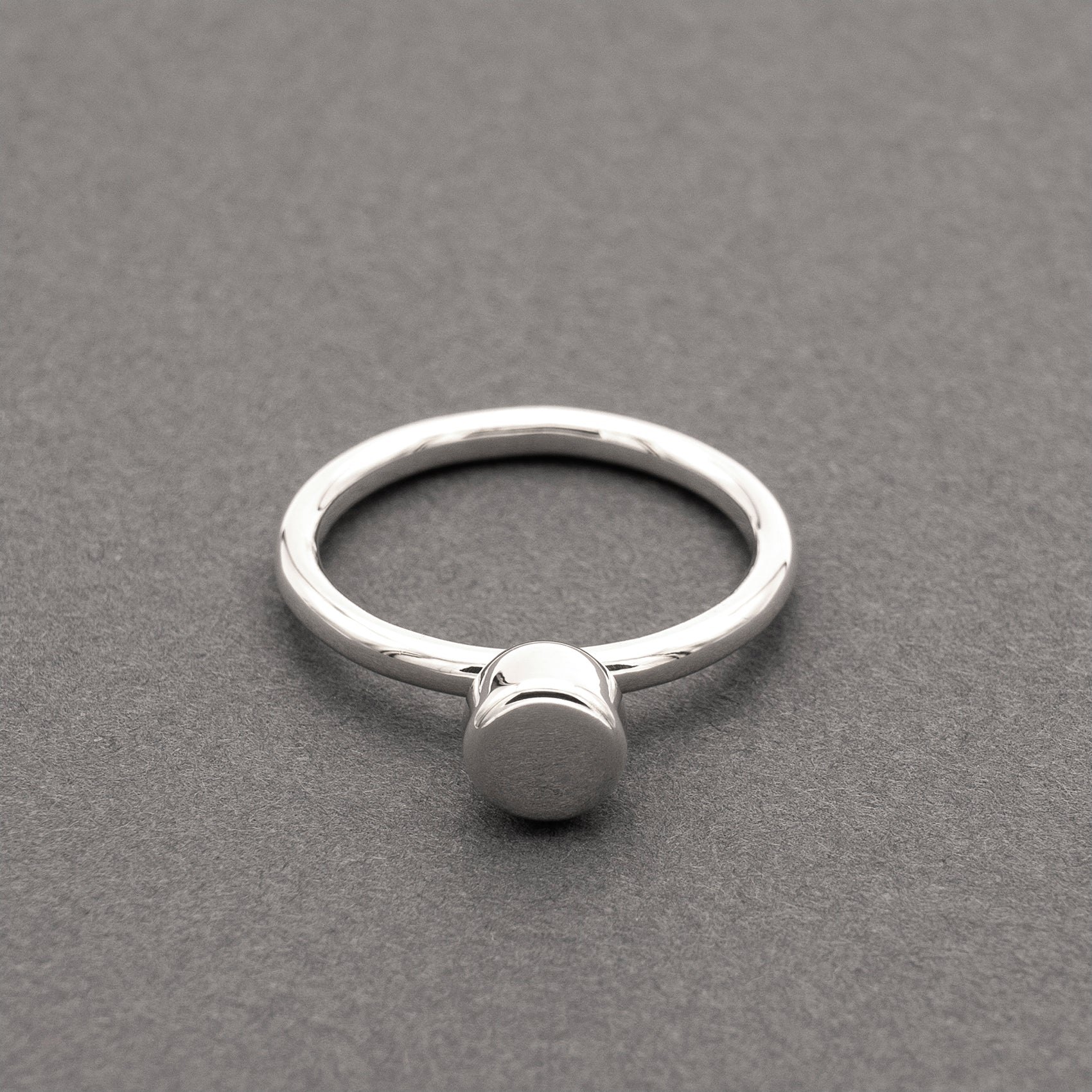 A front view of a silver ring with a minimalist design and a half-capsule element.
