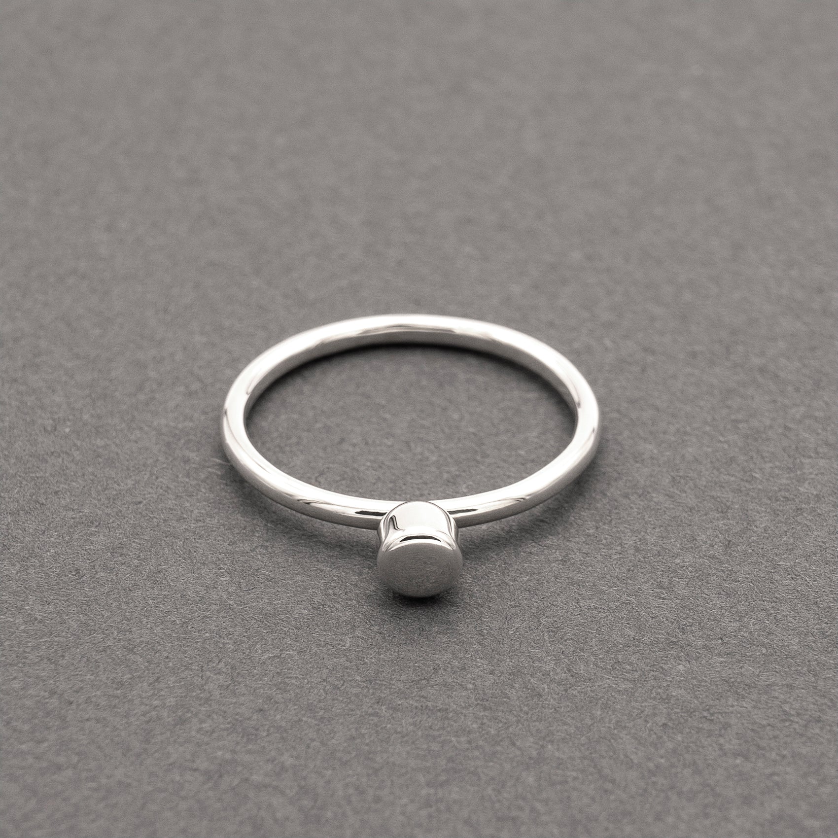 A front view of a silver ring with a minimalist design and a small half-capsule element.