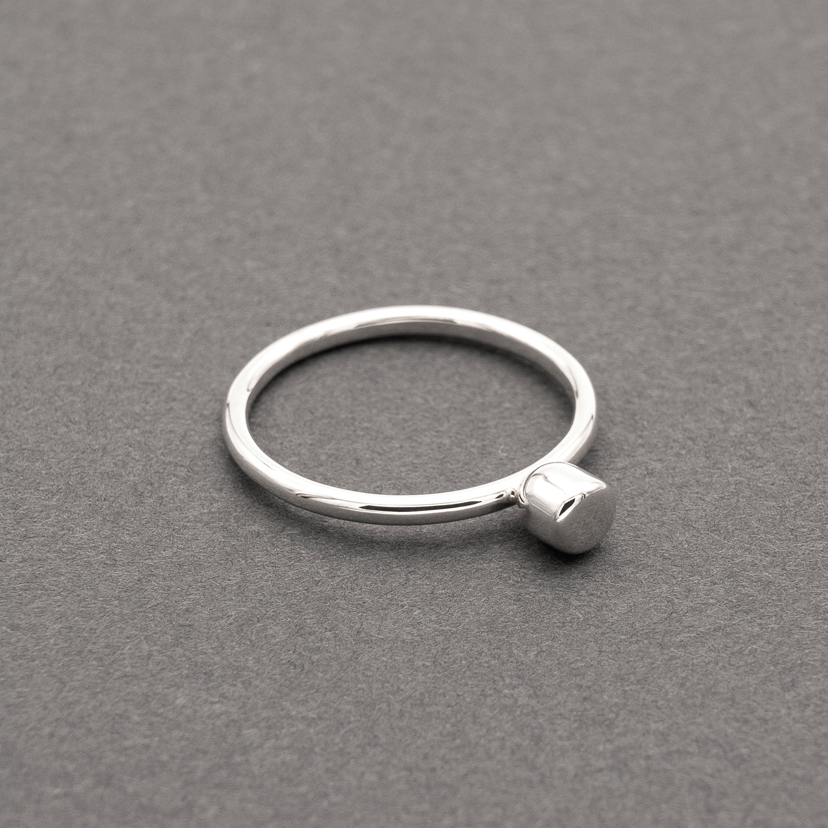 A slight side view of a silver ring with a minimalist design and a small half-capsule element.
