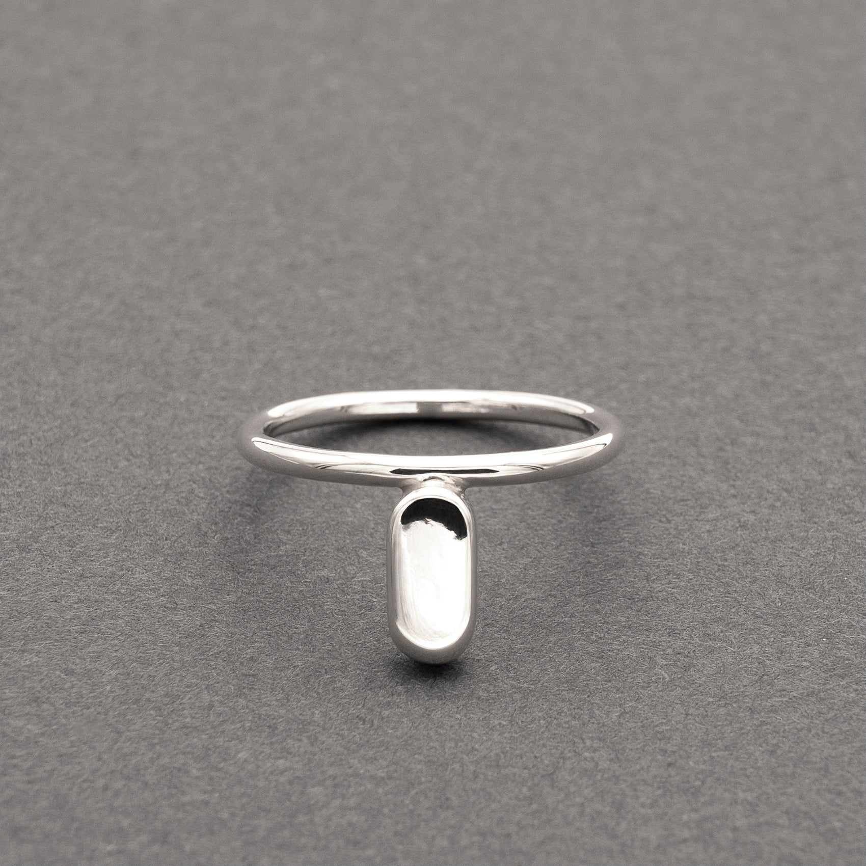 A front view of a silver ring with a minimalist design and a flat capsule element.