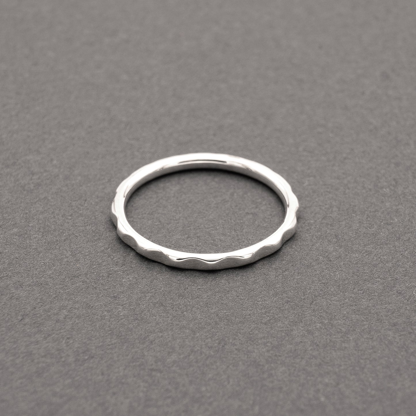 Minimalist design thin silver ring with a wavy texture, displayed on a grey background.