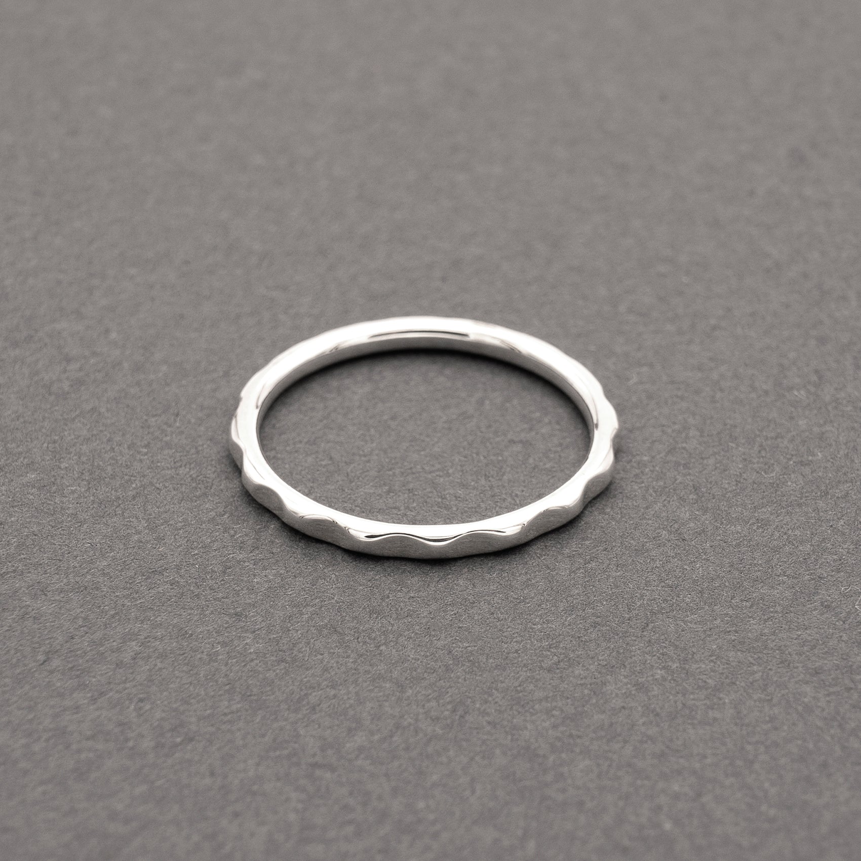 Minimalist design thin silver ring with a wavy texture, displayed on a grey background.