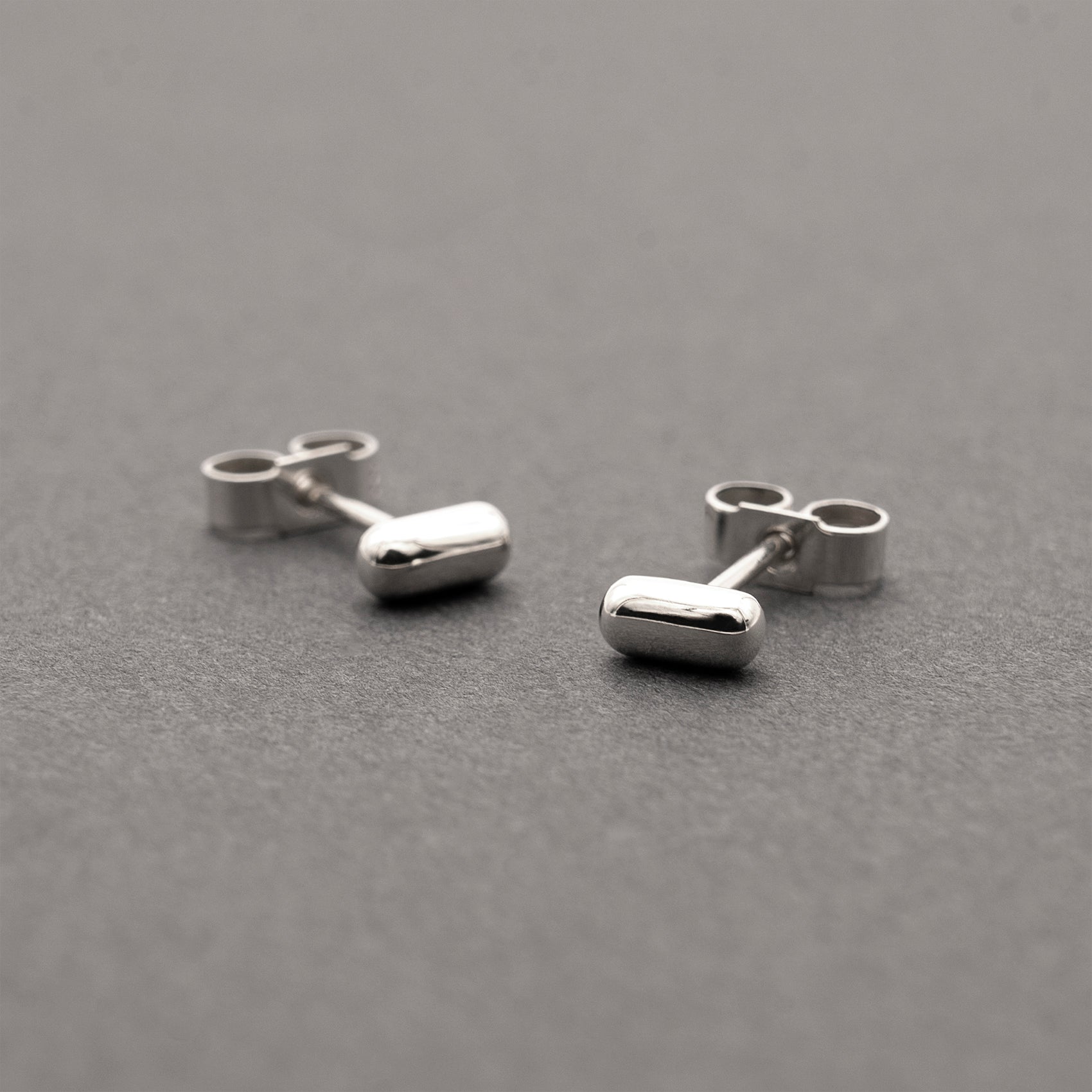 Two silver earrings with a minimalist design in a capsule shape.