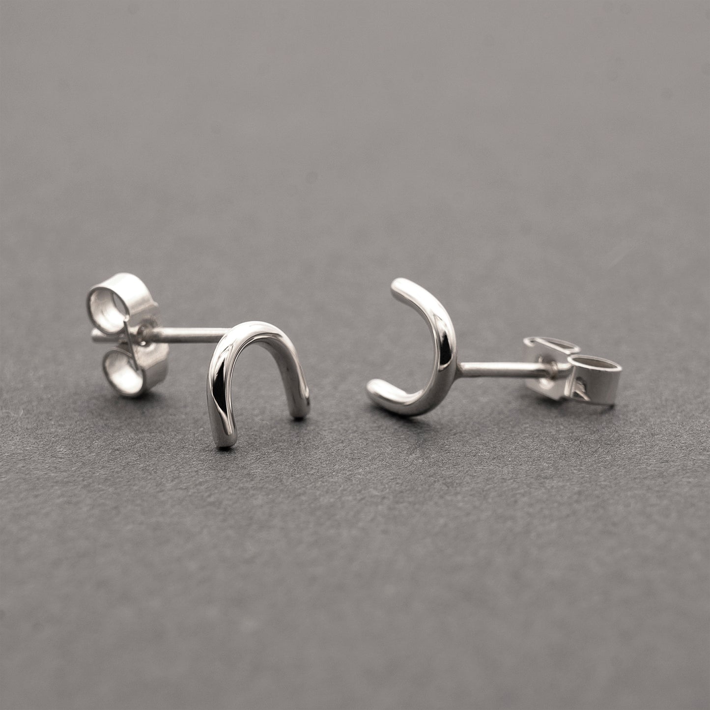  A close-up of two minimalistic silver horseshoe-shaped earrings.