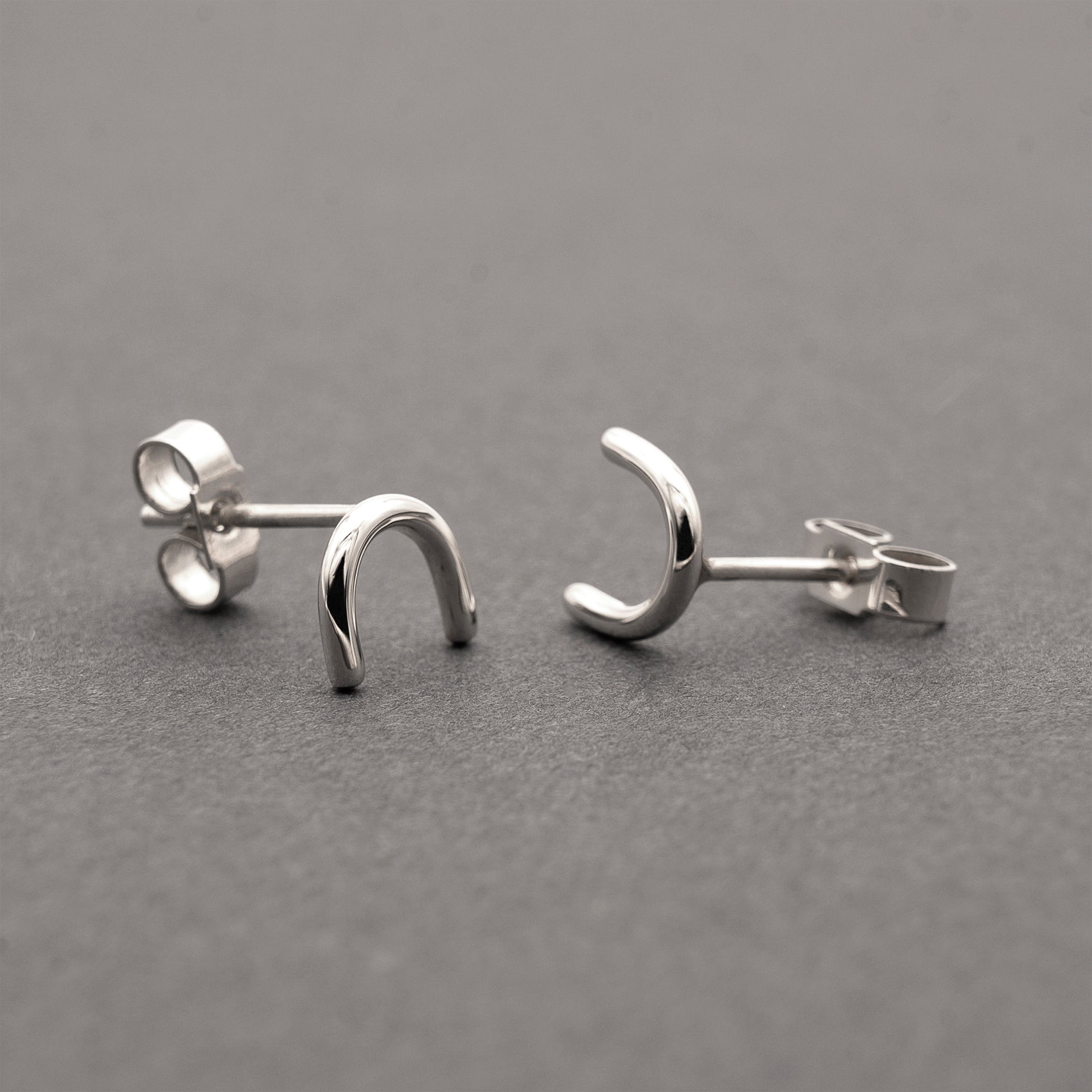  A close-up of two minimalistic silver horseshoe-shaped earrings.