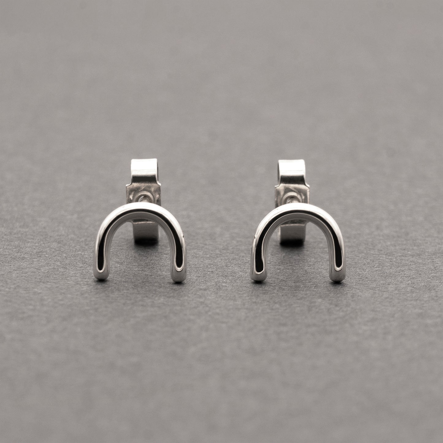 A front view of two minimalistic silver horseshoe-shaped earrings.