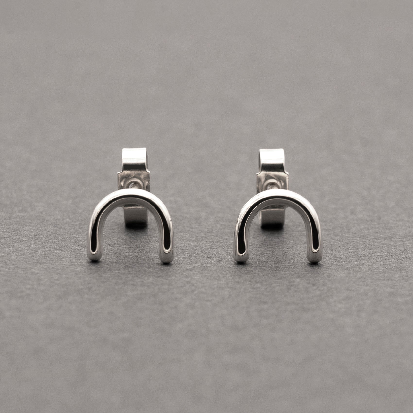 A front view of two minimalistic silver horseshoe-shaped earrings.