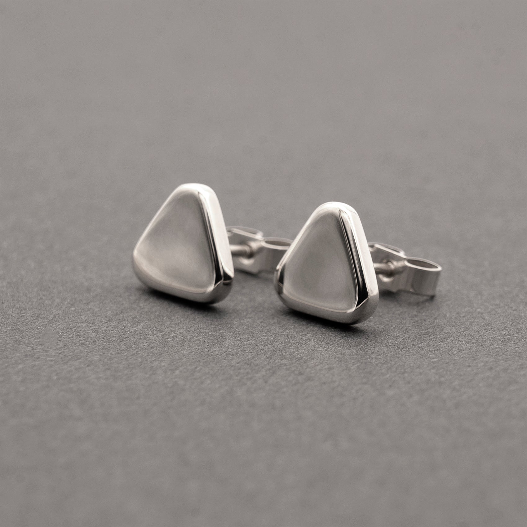 A slight side view of two minimalist design silver earrings in a soft triangular shape.