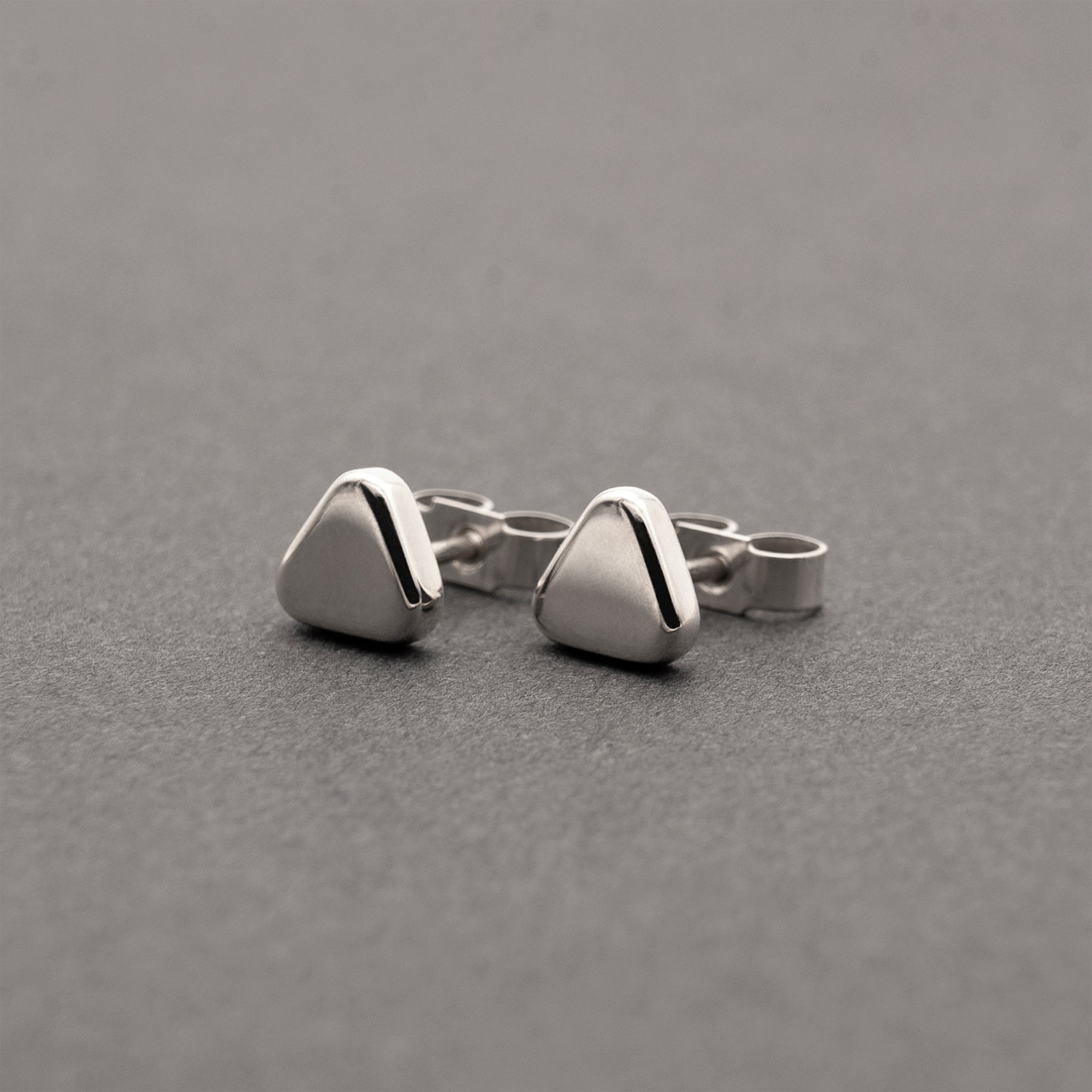 A slight side view of two small minimalist design silver earrings in a soft triangular shape.