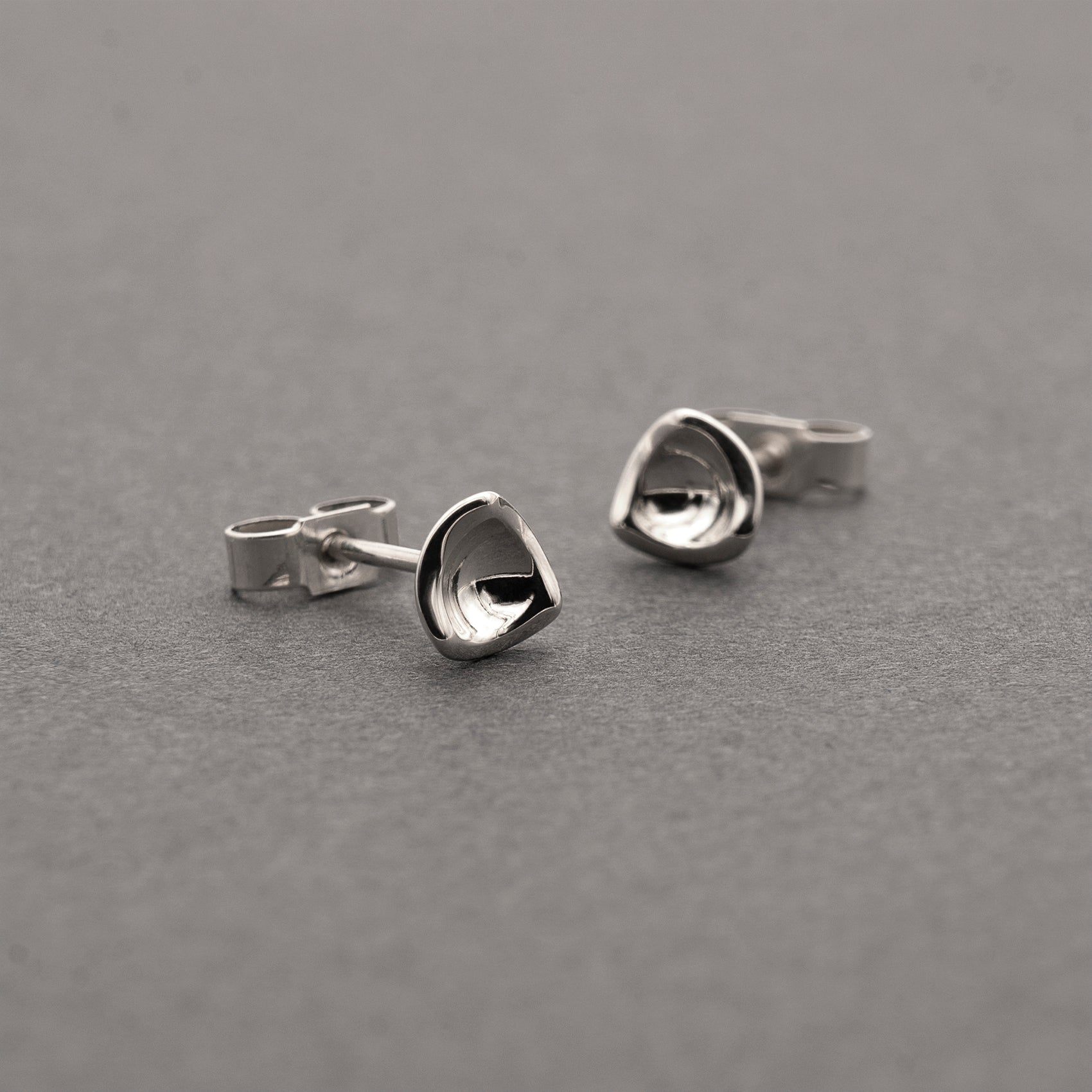 Two small silver earrings in a minimalist, organic shape.
