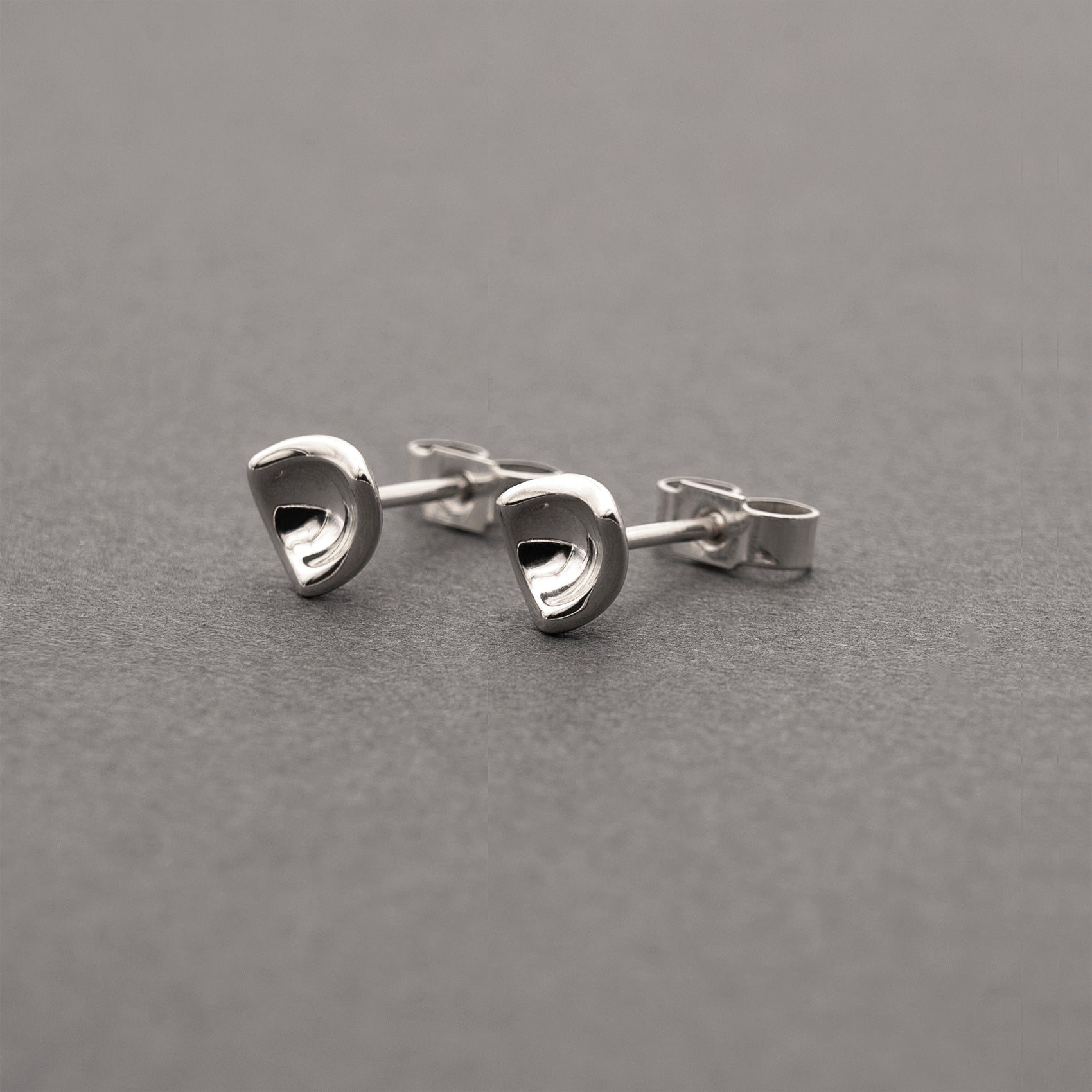 A slight side view of two small silver earrings in a minimalist, organic shape.