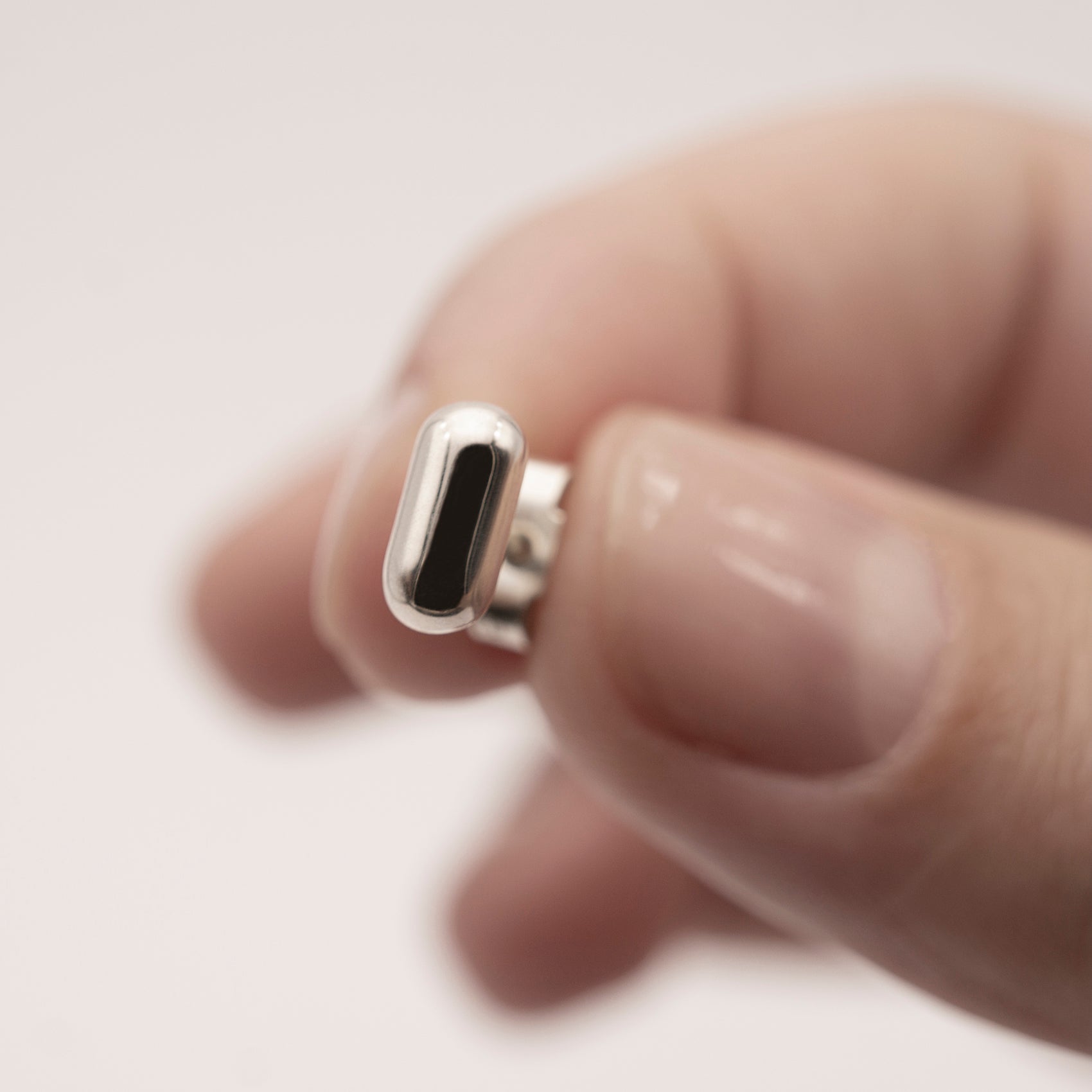 A close-up of a silver earring with a minimalist design in a capsule shape in a woman's hand.