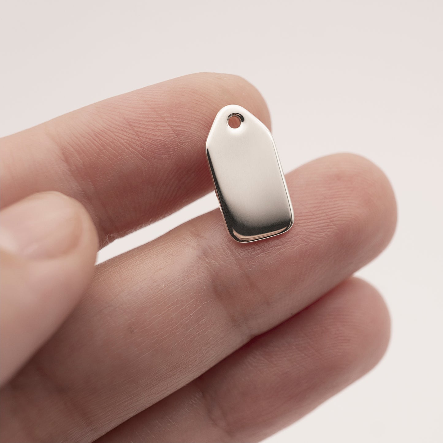 A close-up of a minimalist silver earring backplate in a woman's hand.