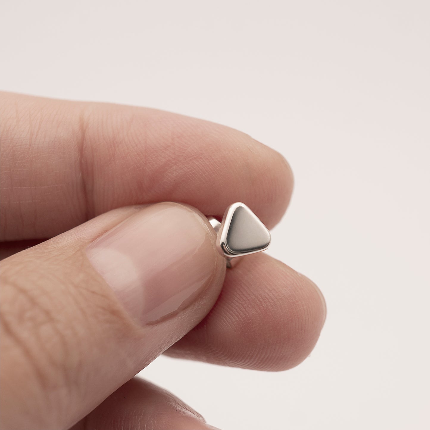 A close-up of a small minimalist design silver earring in a soft triangular shape in a woman's hand.