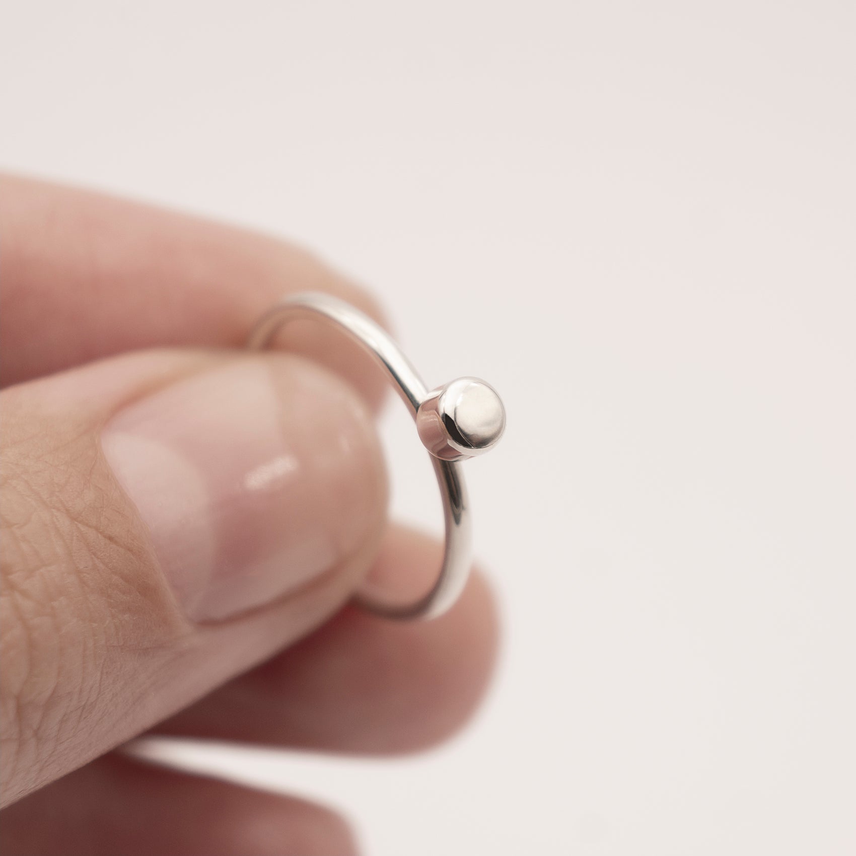 A close-up of a minimalist design silver ring with a small half-capsule element in a woman's hand.