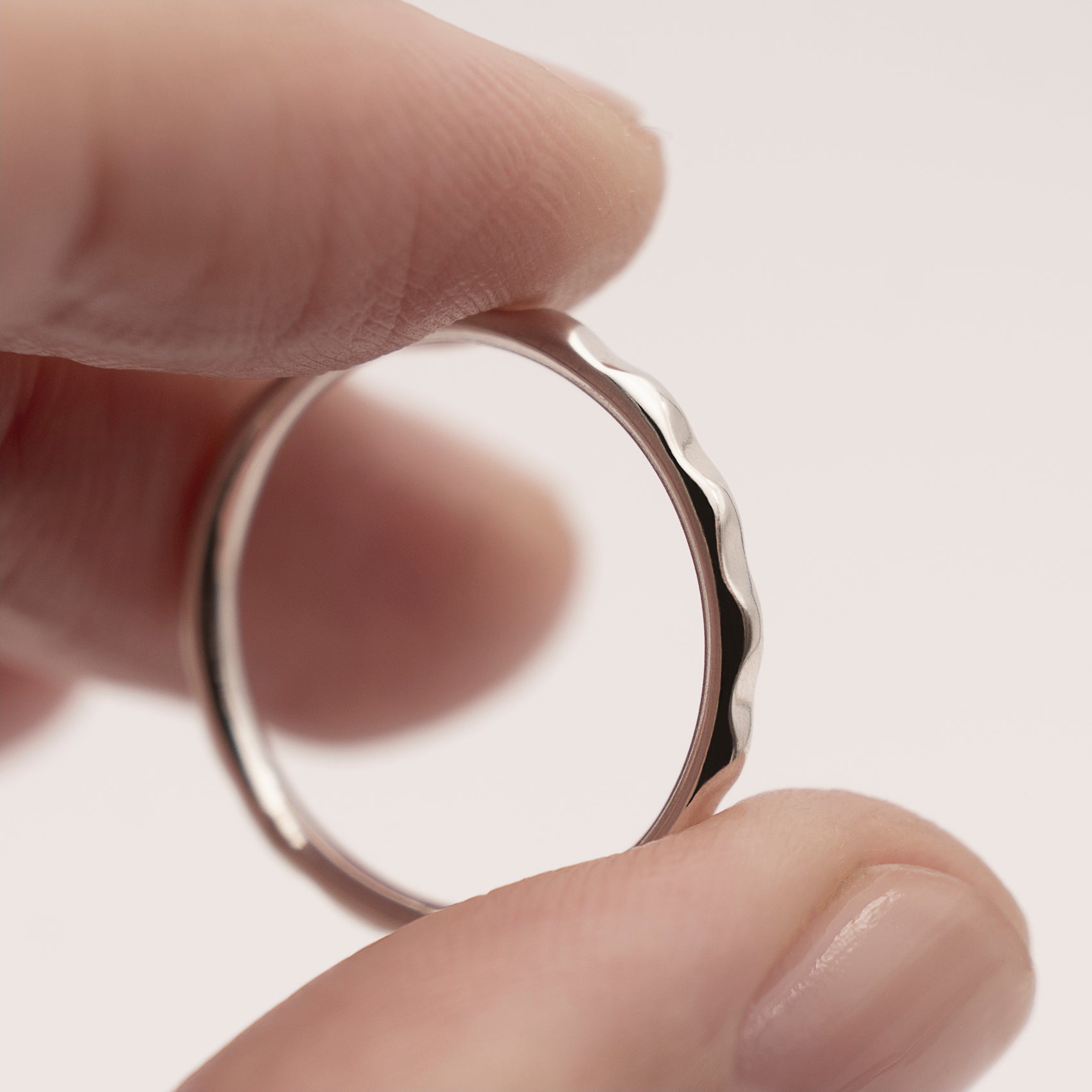 A close-up of a minimalist design thin silver ring with a wavy texture in a woman's hand.